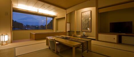 Une pièce de style japonais traditionnel, avec un sol recouvert de tatamis, une table basse, un téléviseur et une vue sur une montagne.