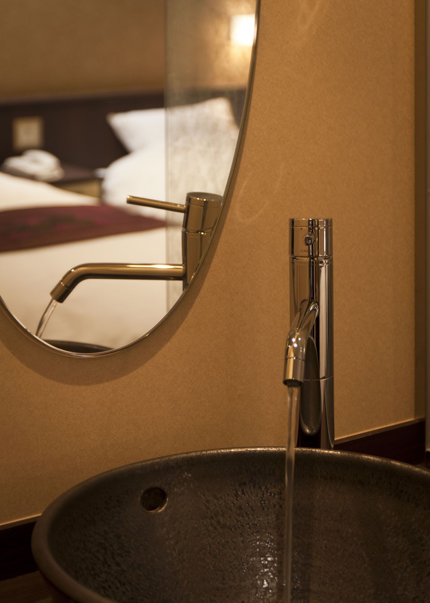 A bathroom sink with a modern faucet and a round mirror reflecting the room.