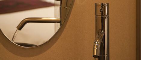 A bathroom sink with a modern faucet and a round mirror reflecting the room.