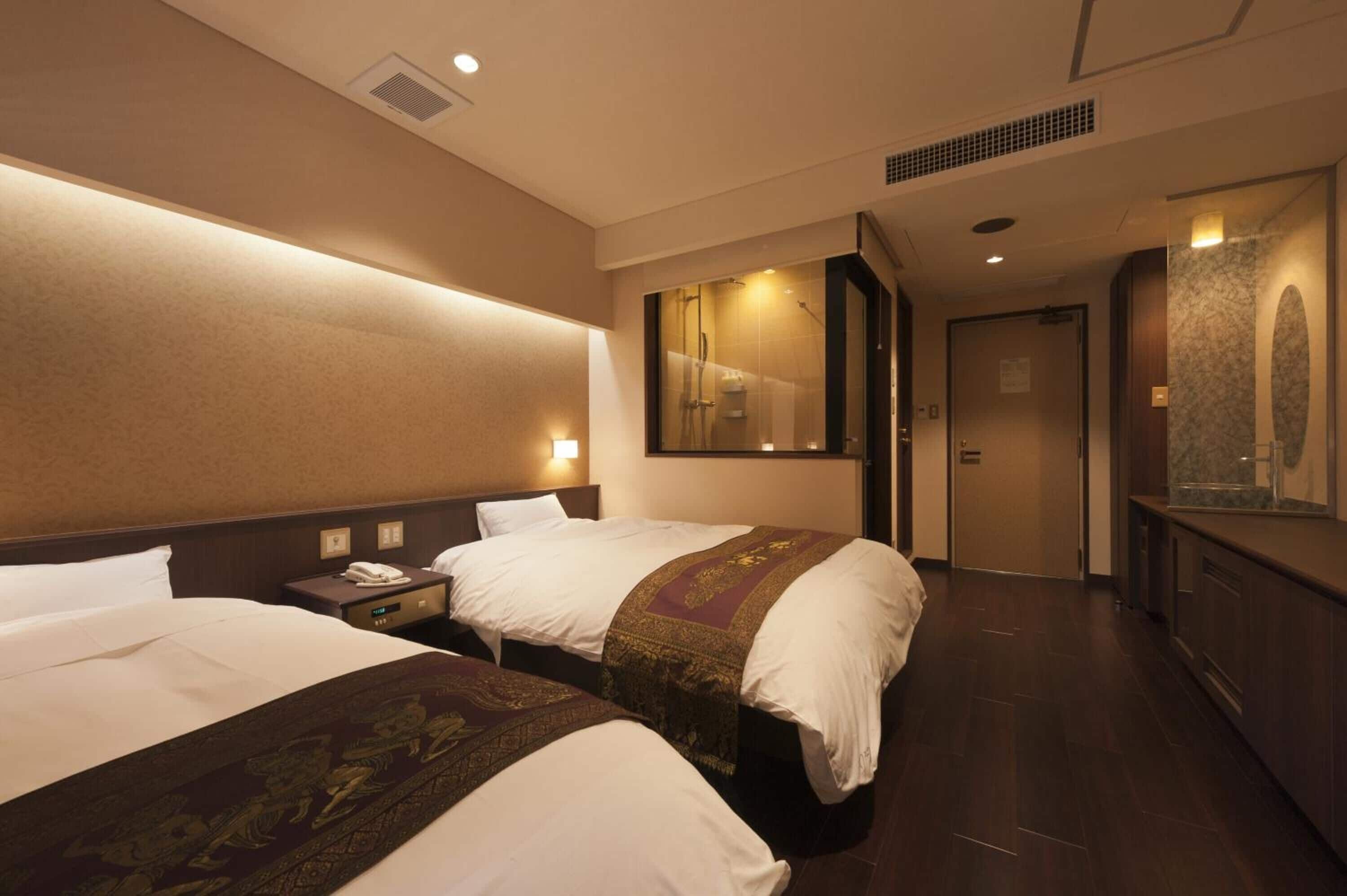 Habitación de hotel con dos camas, una mesita de noche, un espejo y un baño con ducha.