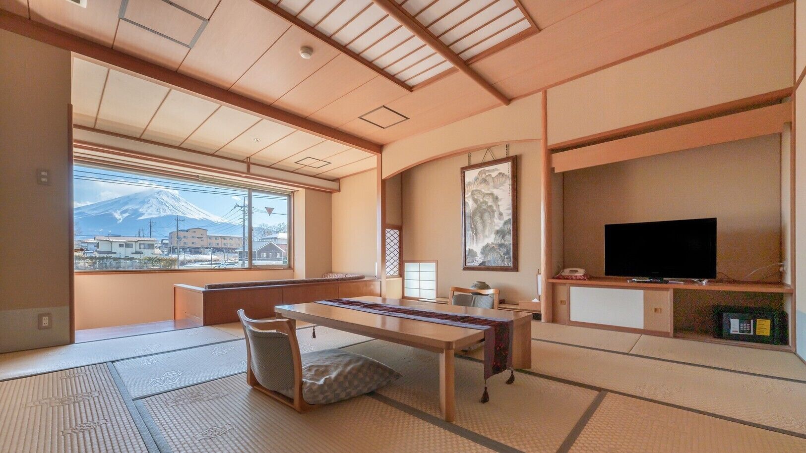 Ett traditionellt japanskt rum med tatamimattor på golvet, ett lågt bord, en tv och utsikt över ett berg.