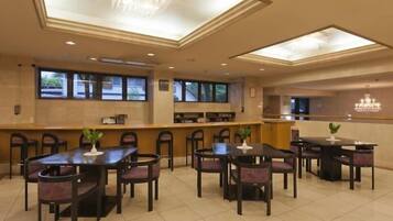 A hotel dining area with multiple tables and chairs, a reception desk, and large windows.