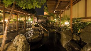 Un jardín interior tranquilo con fuente de agua, senderos de piedra y construcciones de madera.