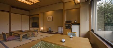 Una habitación tradicional japonesa con suelo de tatami, una mesa baja con un juego de té, un televisor y vistas a zonas verdes.