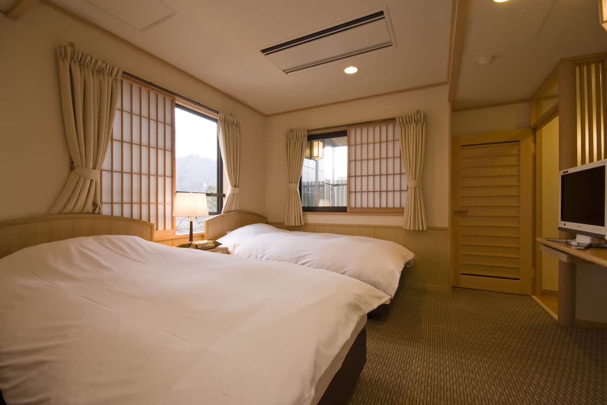 A hotel room with two beds, a TV, a desk, and a window with curtains.