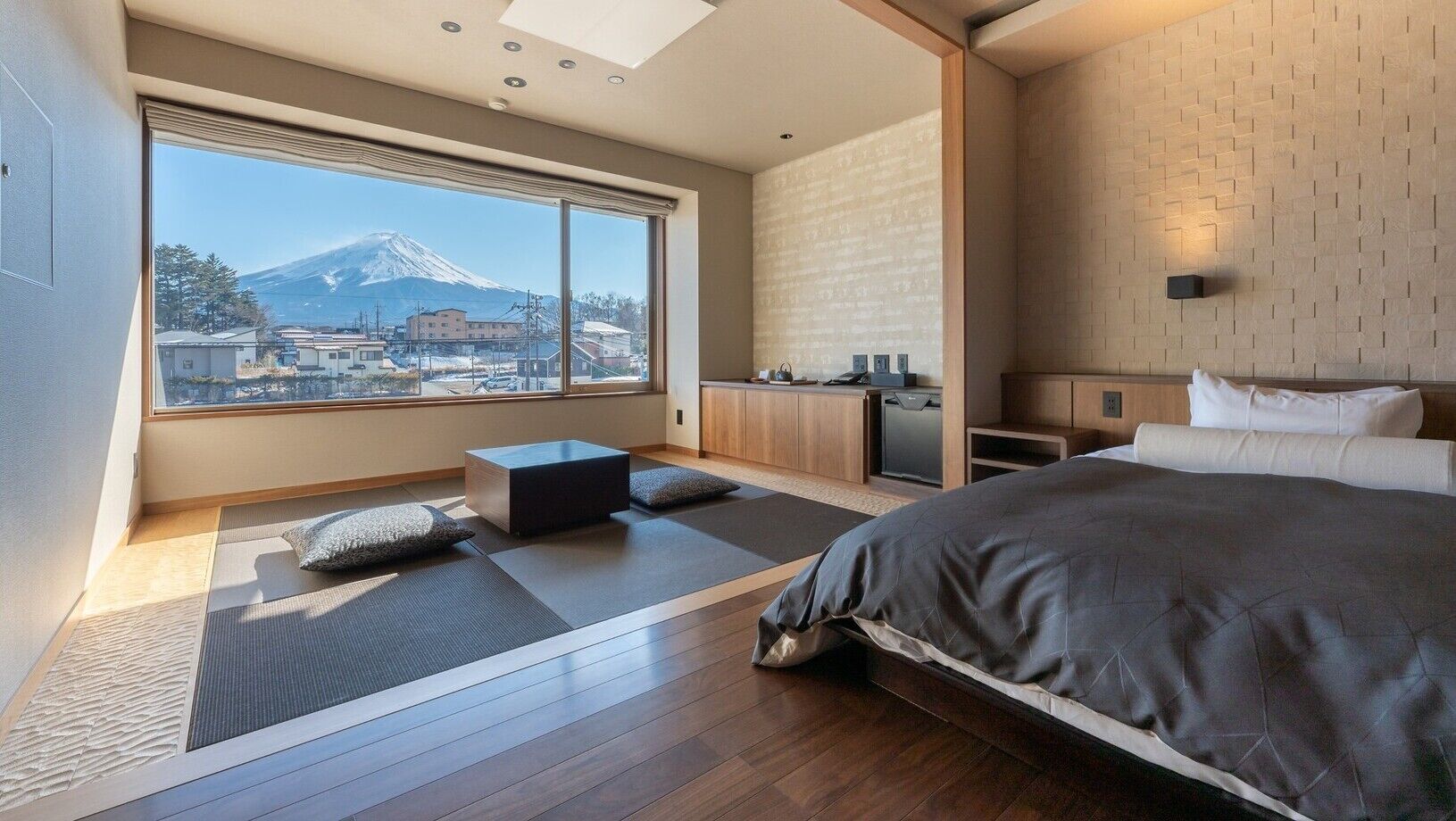 A modern hotel room with a large bed, a small seating area, a kitchenette, and a view of a mountain.