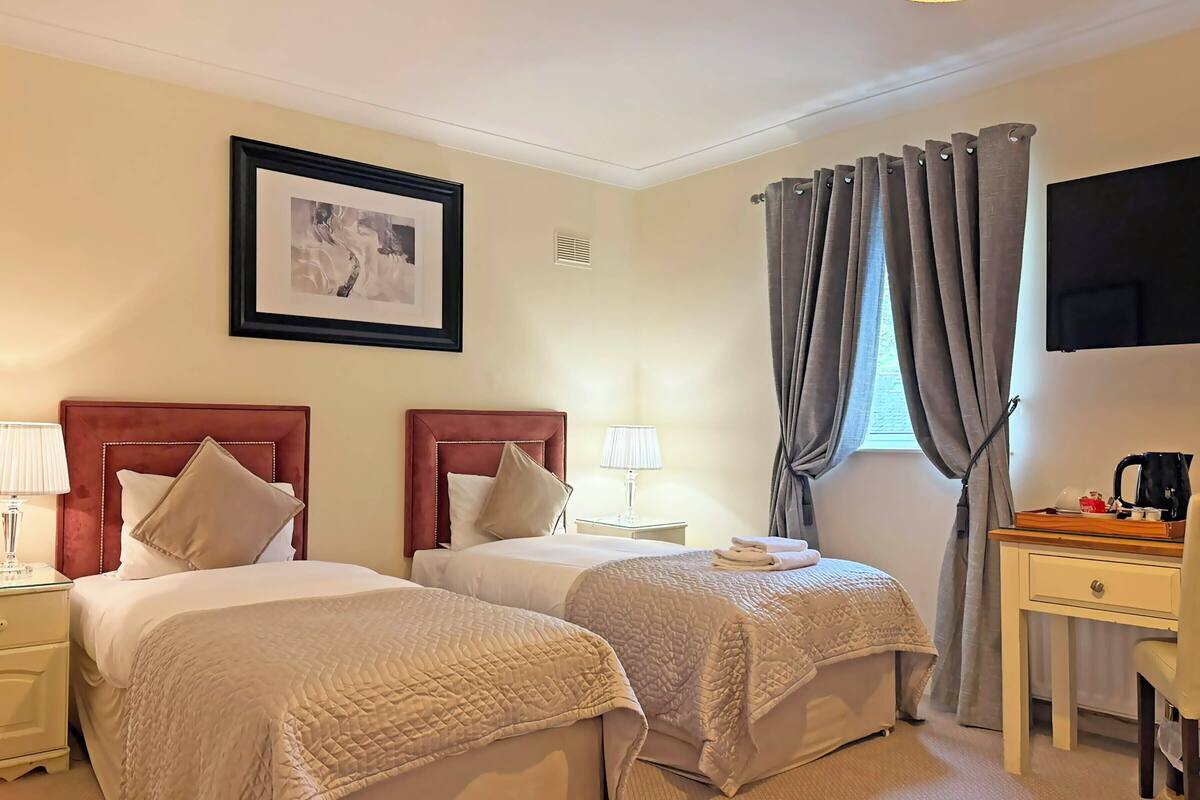 A hotel room with two beds, a desk, a chair, a TV, and a window with curtains.