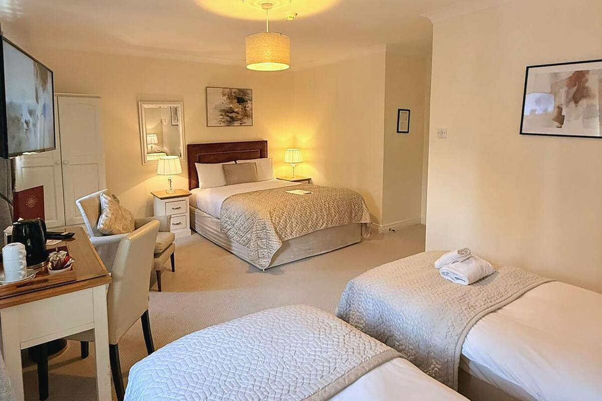 A hotel room with two single beds, a desk with a chair, a lamp, and a painting on the wall.
