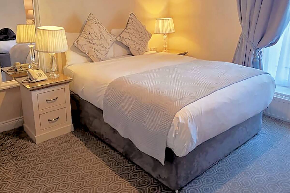 A hotel room with a bed, bedside lamps, a telephone, a mirror, and a patterned carpet.