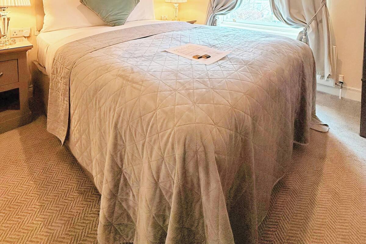A hotel room with a large bed, two bedside tables with lamps, a painting on the wall, and a window with curtains.