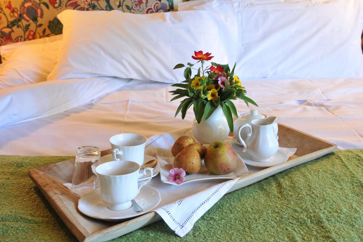 A breakfast tray with a vase of flowers, a teapot, cups, and apples on a bed.
