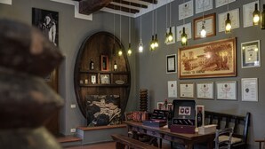 Een kamer met een houten bank, een tafel en een muur versierd met ingelijste diploma’s en een groot schilderij.