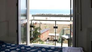 Una habitación con cama, ventana con vista a la playa y balcón con mesa y sillas.