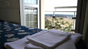 Una cama con un edredón azul y una toalla blanca, junto a una ventana con vistas a la playa.