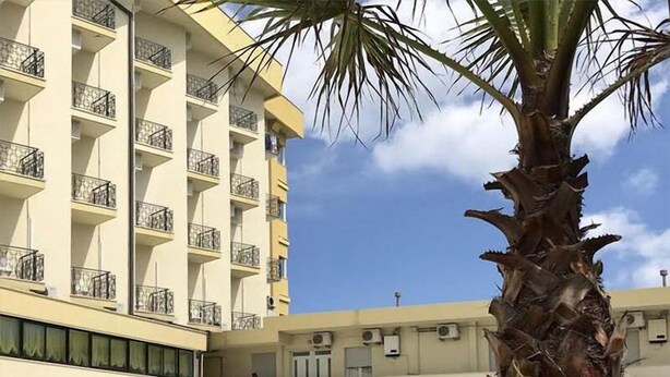 Un hotel con zona de piscina, incluyendo sillones de descanso y sombrillas, y una palmera.