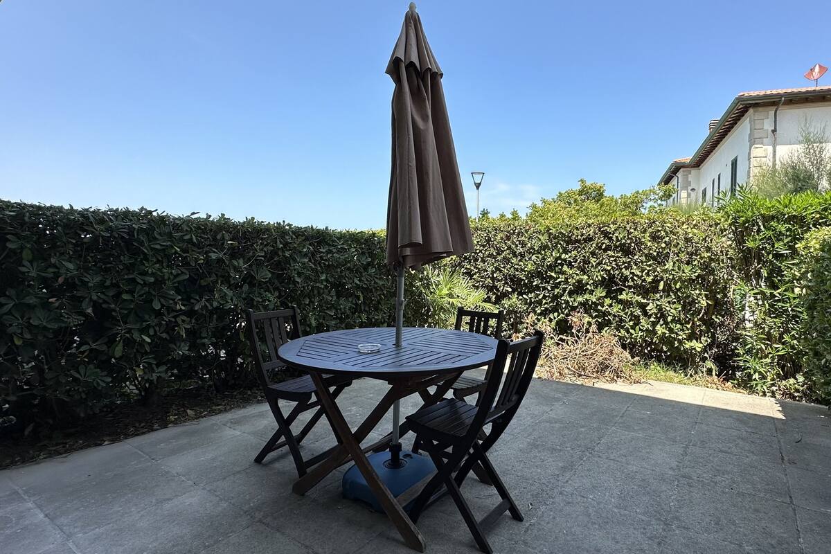 A round patio table with four chairs and a brown umbrella.