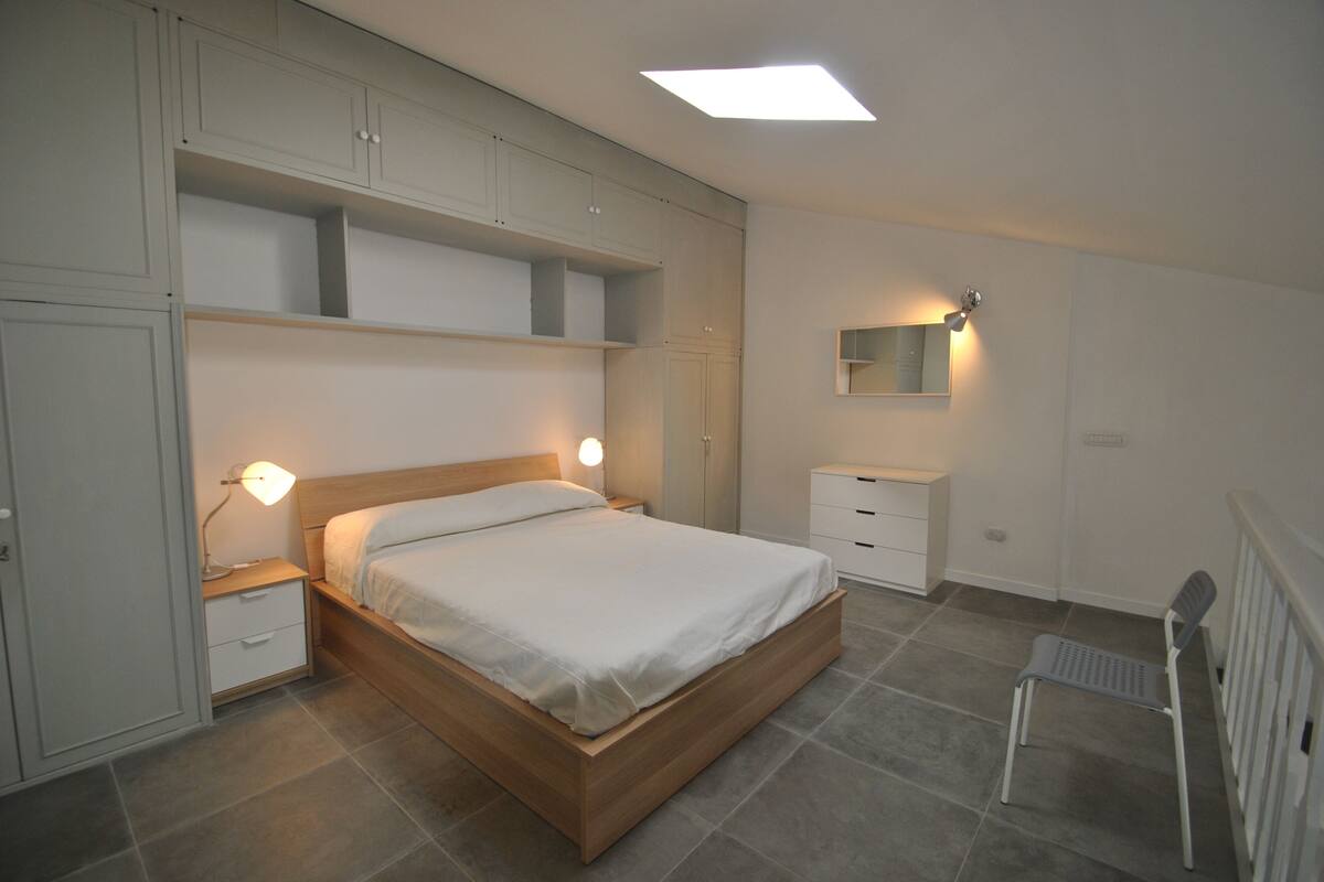 A bedroom with a wooden bed, bedside lamps, a nightstand, a small white dresser, and a radiator.