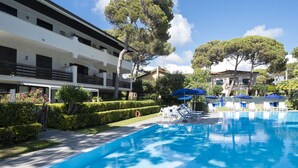 A pool area with lounge chairs and umbrellas, surrounded by neatly trimmed hedges and trees. - Fattoria nel Parco (Rosignano Marittimo)