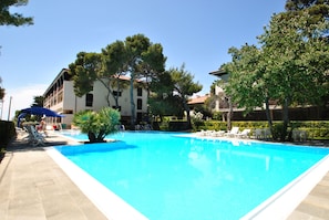 A swimming pool with lounge chairs and umbrellas, surrounded by trees and buildings. - Fattoria nel Parco (Rosignano Marittimo)