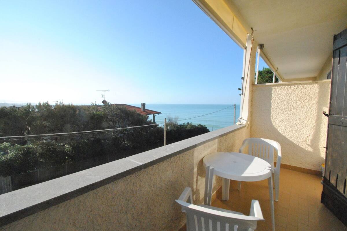 A balcony with a view of the sea, a white table, and two white chairs.
