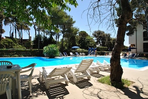 A swimming pool with lounge chairs and a table, surrounded by trees and a building. - Fattoria nel Parco (Rosignano Marittimo)