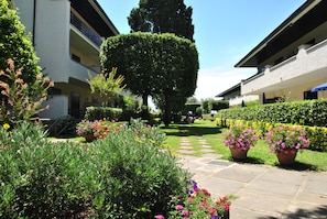 A courtyard with a central pathway, surrounded by neatly trimmed hedges and potted plants with flowers. - Fattoria nel Parco (Rosignano Marittimo)