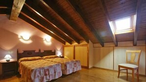 A room with two beds, wooden flooring, a skylight, and a chair. - Picu Castiellu Aparthotel (Llanes)