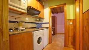 A compact kitchen with wooden cabinets, a washing machine, and a microwave. - Picu Castiellu Aparthotel (Llanes)