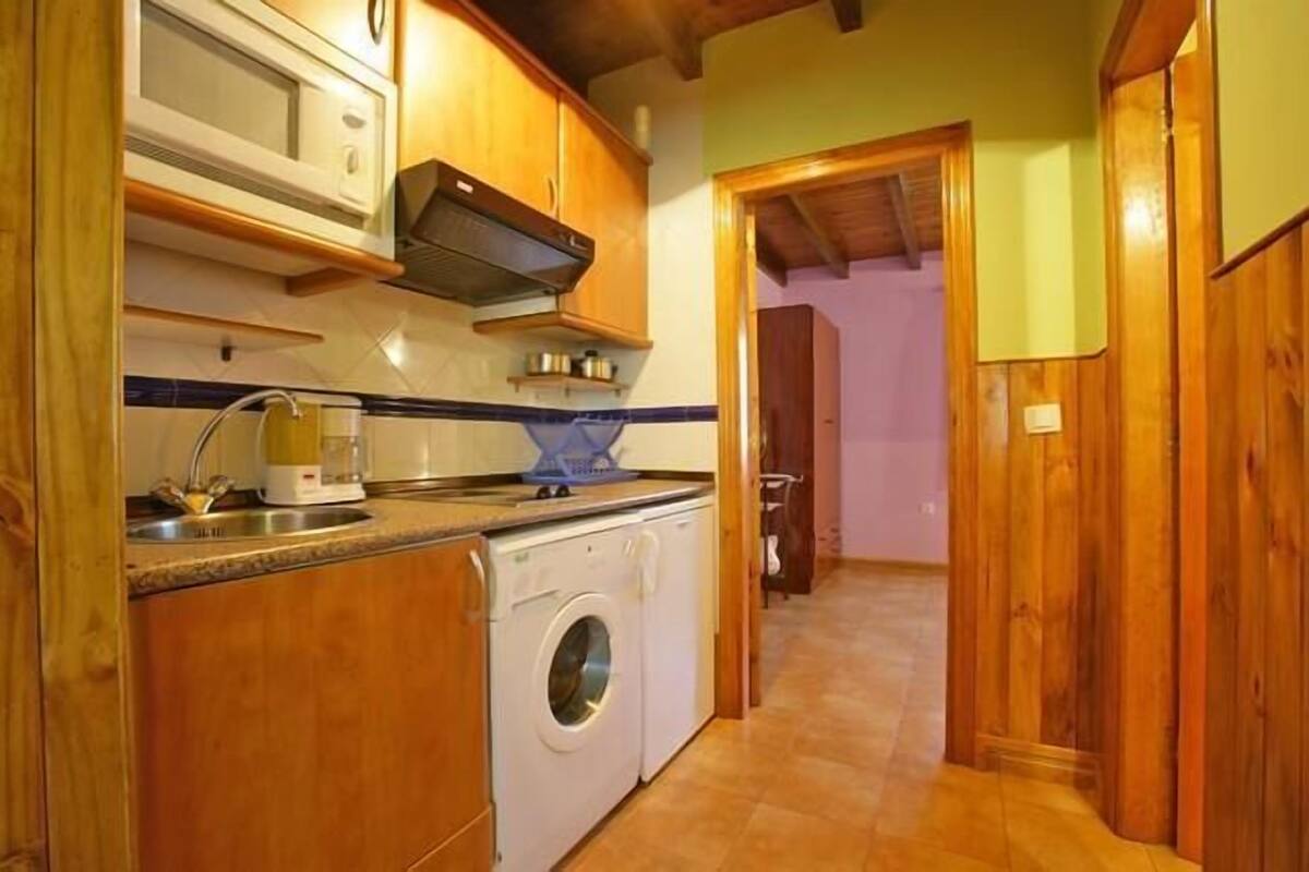 Una cocina compacta con armarios de madera, lavadora y microondas.