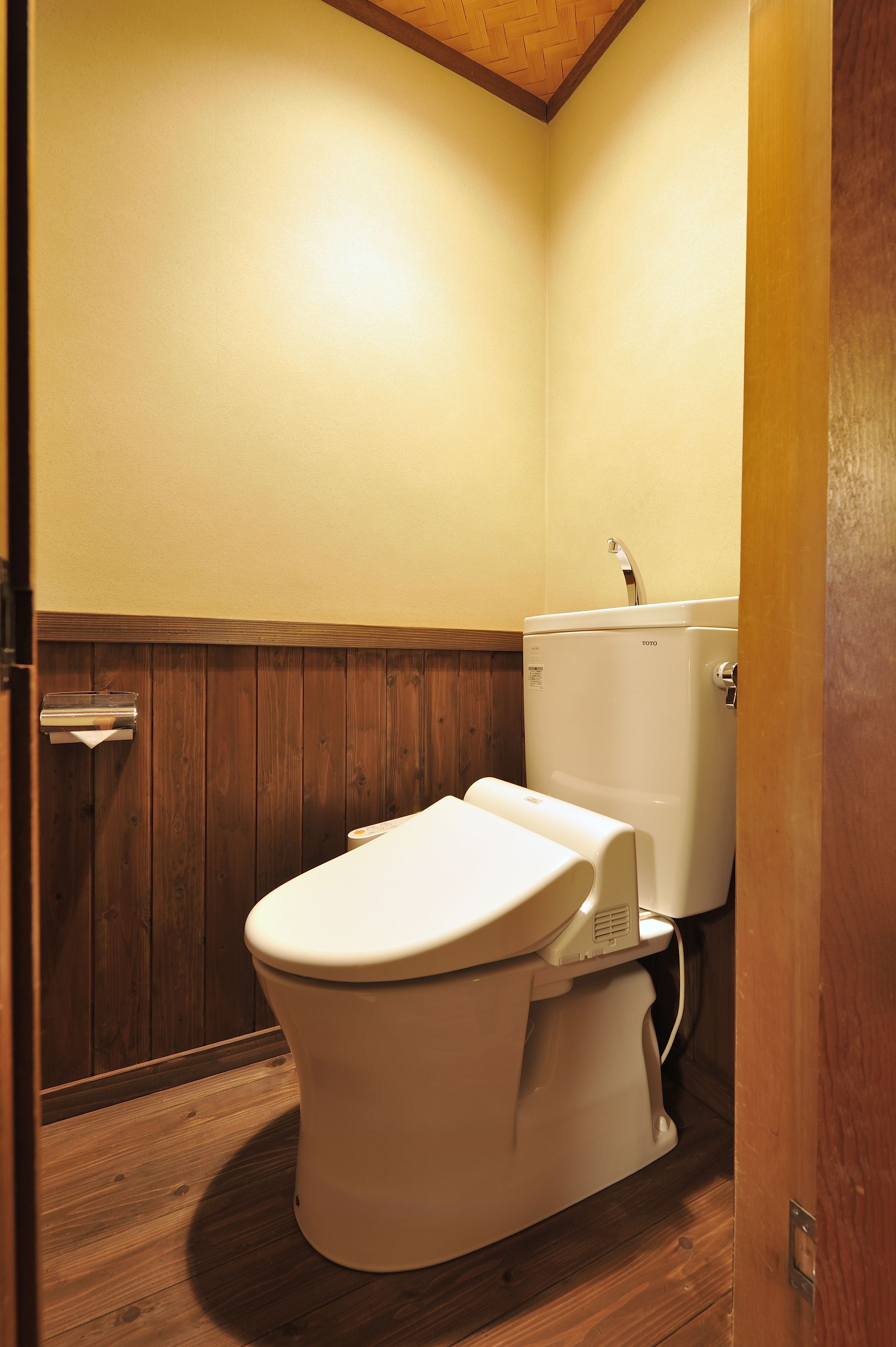 Een kleine, compacte badkamer met een houten vloer, een wit toilet en een wastafel aan de muur.