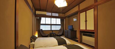 Habitación de hotel con dos camas, un escritorio, una silla y un televisor.