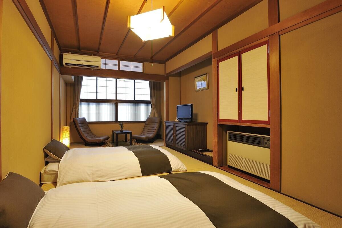 Habitación de hotel con dos camas, un escritorio, una silla, un televisor y un armario.