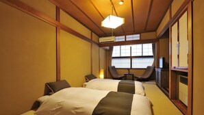 A traditional Japanese-style hotel room with tatami flooring, two beds with white and dark bedding, a ceiling fan, and a television. - Hodakaso Yamanoiori (Takayama)