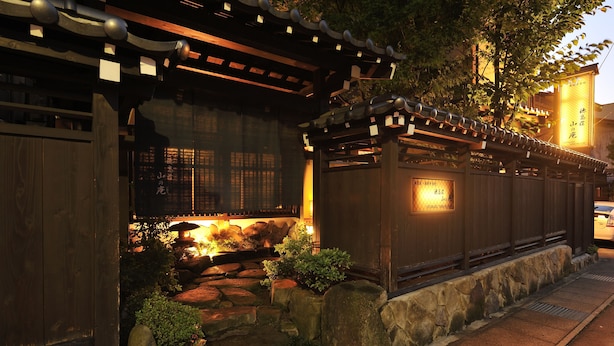 A traditional Japanese building with a wooden entrance, stone pathway, and a lit lantern. - Hodakaso Yamanoiori (Takayama)