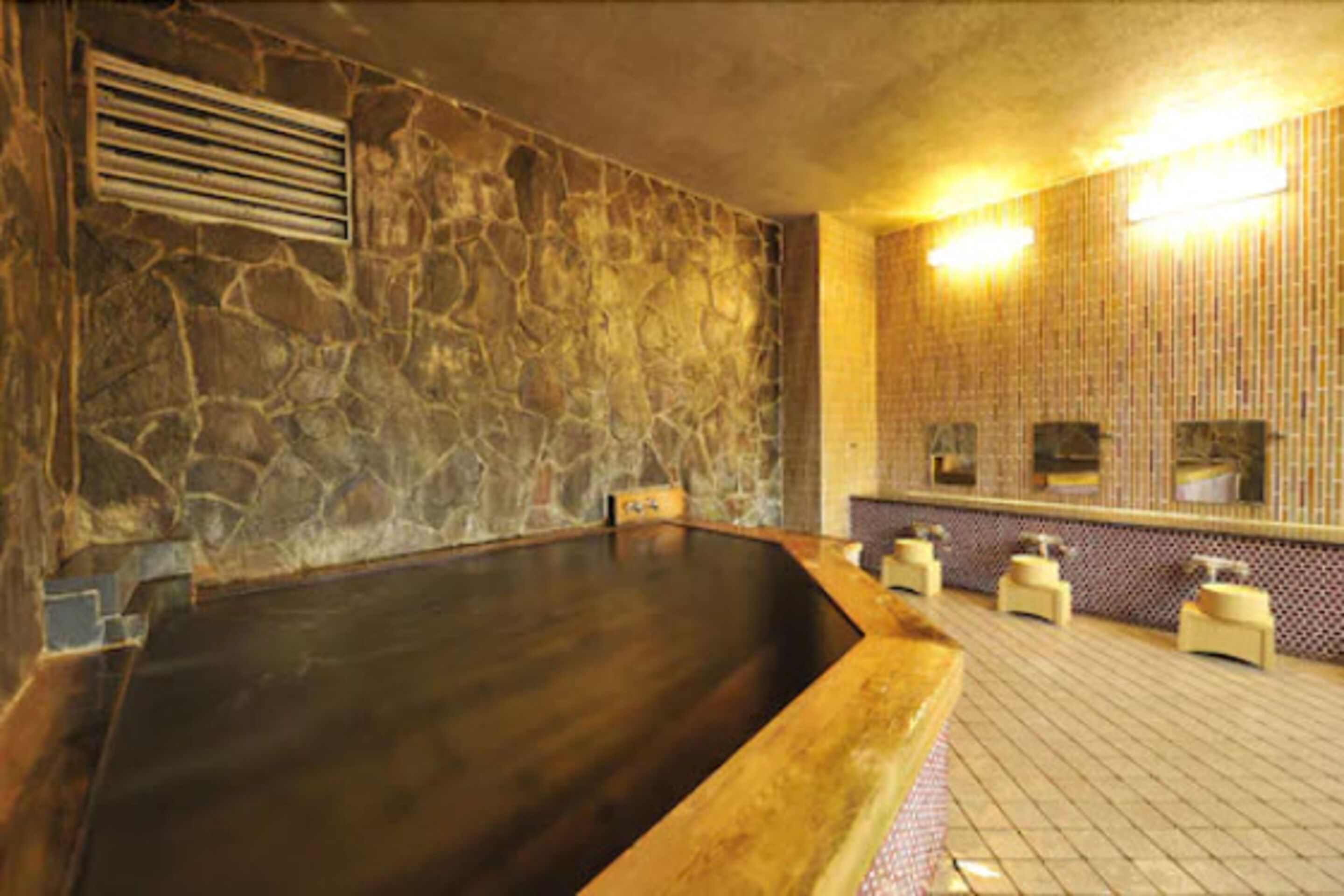 A stone-walled room with a large wooden bathtub, a stone bench, and a tiled floor.