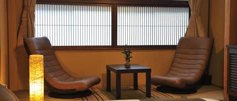 A room with two leather recliners, a small table with a vase, and a bed.