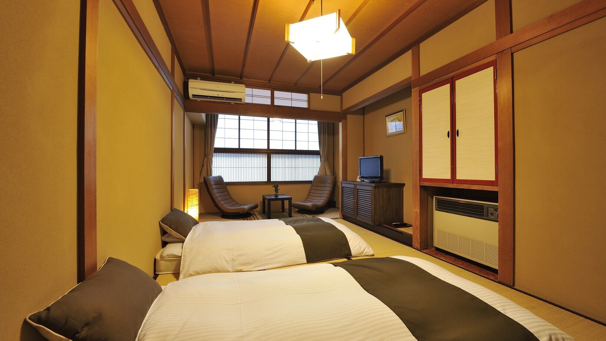 Een hotelkamer met twee bedden, een televisie, een bureau, een stoel en een traditionele Japanse kast.