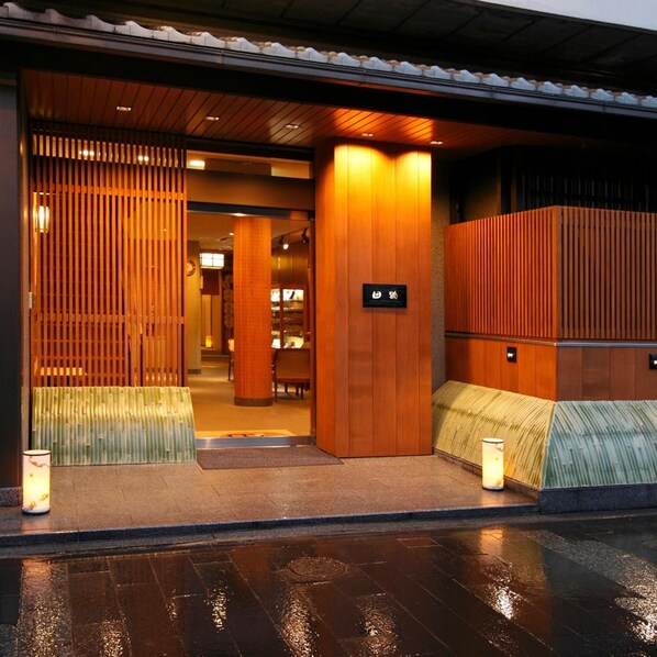 A hotel entrance with a wooden facade, a reception desk, and a sign indicating the hotel's name. - Tazuru (Kyoto)