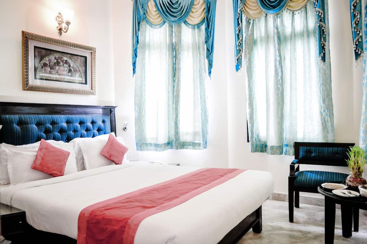 A hotel room with a large bed, a headboard, a framed picture on the wall, and curtains.
