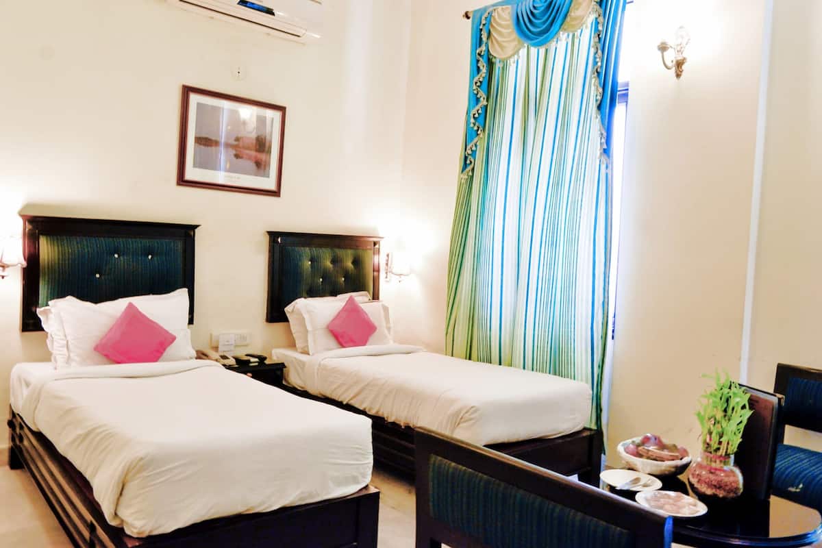 A hotel room with two single beds, a small table with a vase and a bowl, and a chair.