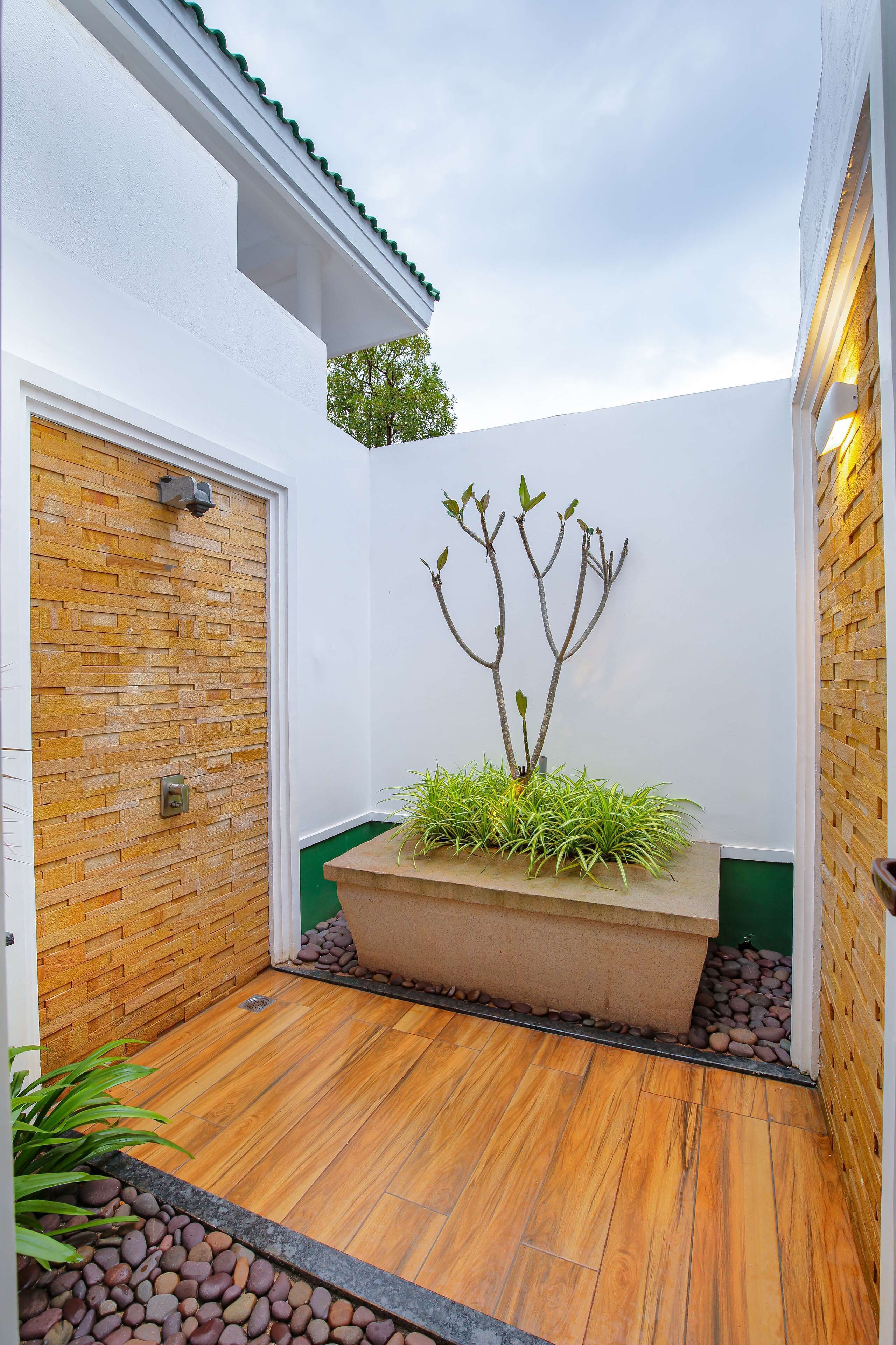 Uma área externa moderna com piso de madeira, parede de tijolos e um vaso com plantas verdes.