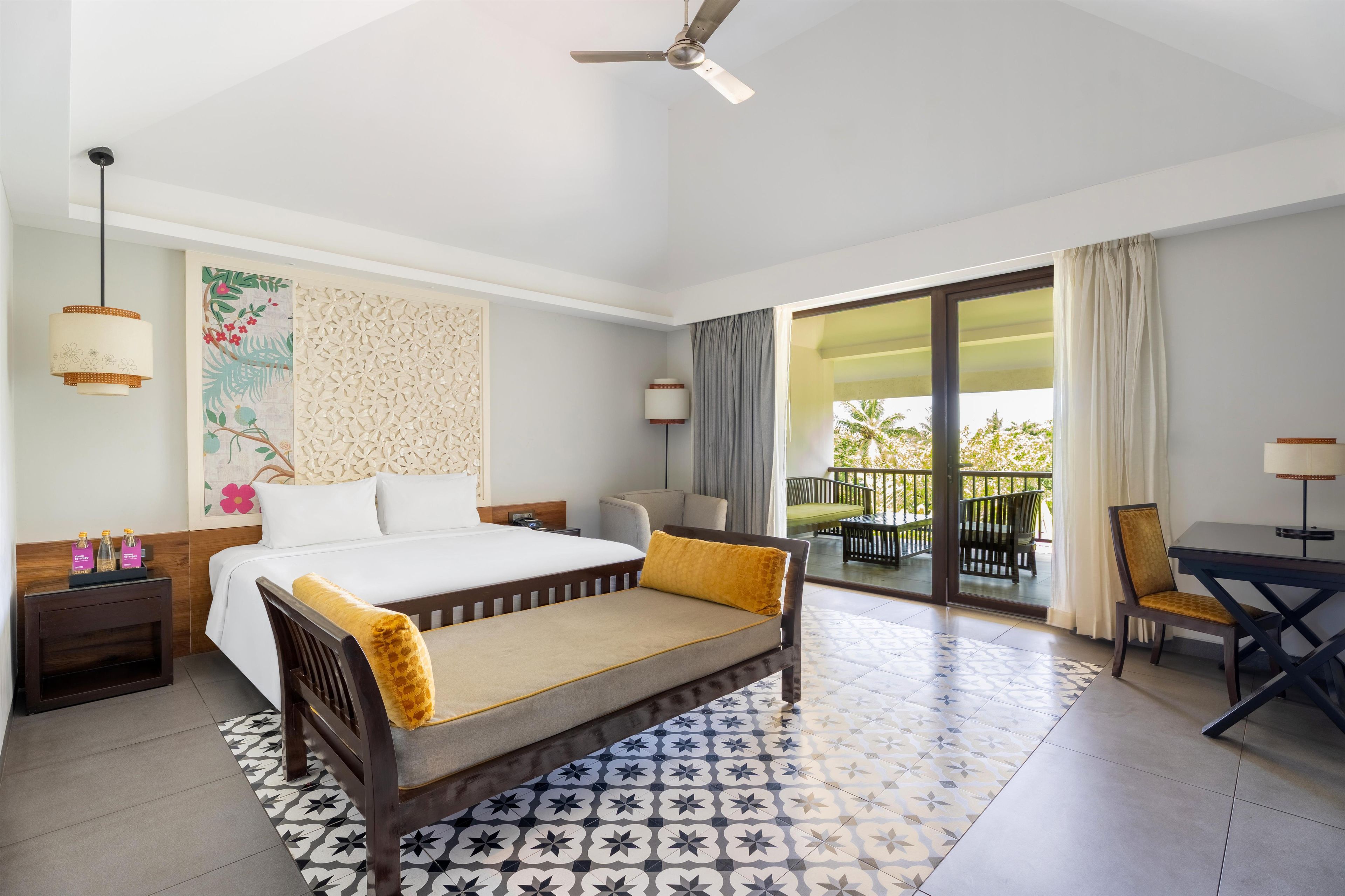 Una habitación de hotel con cama, escritorio, silla, balcón y ventilador de techo.
