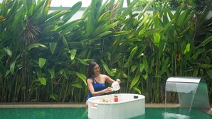 Una mujer con traje de baño azul junto a una piscina con un jacuzzi flotante blanco y una fuente.