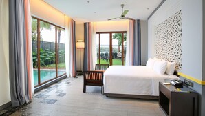 Habitación de hotel con una cama grande, un escritorio y una silla. Tiene una ventana con cortinas, un ventilador de techo y vistas a una piscina y follaje exterior.