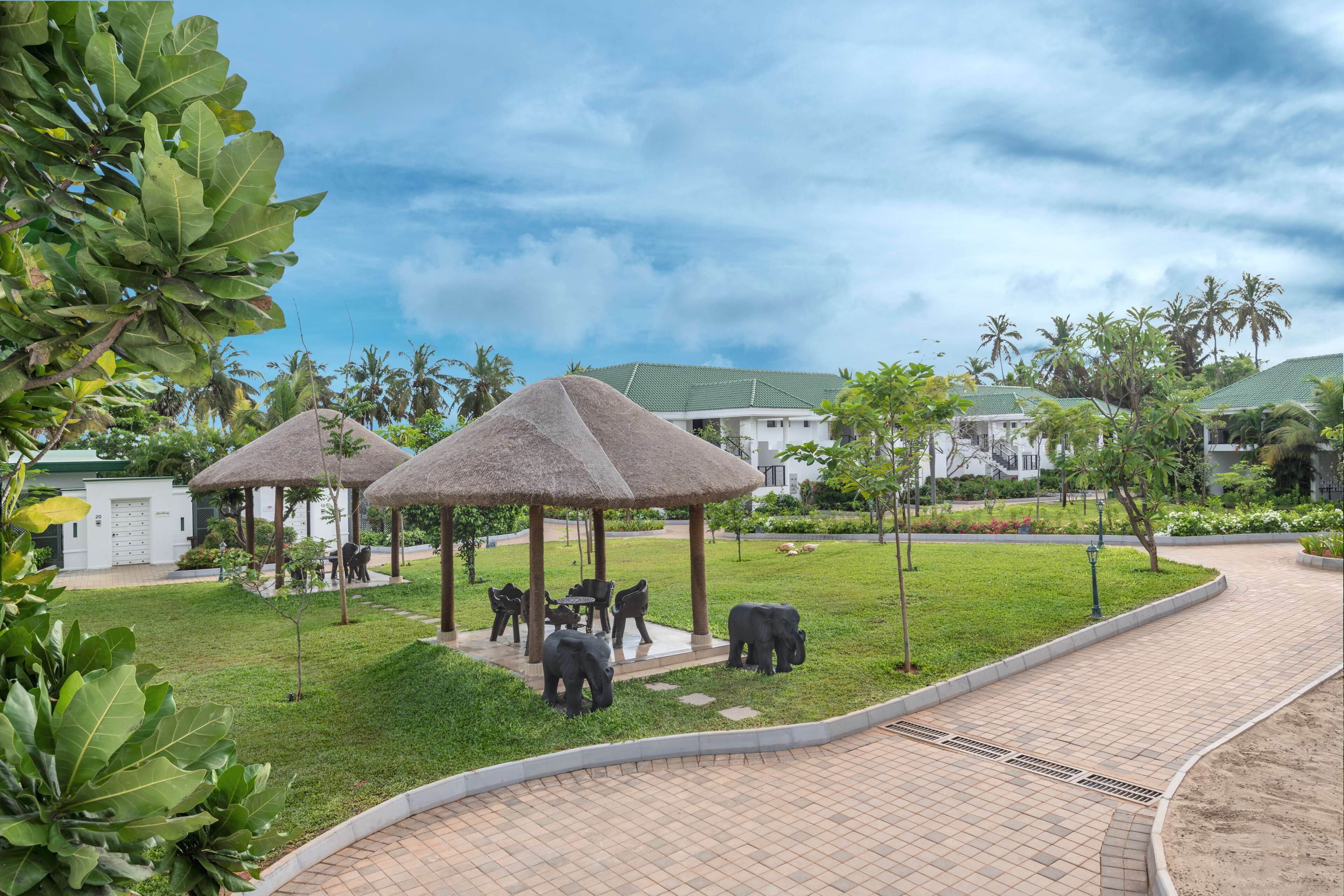 A landscaped area with thatched-roof structures, a paved walkway, and elephant statues.
