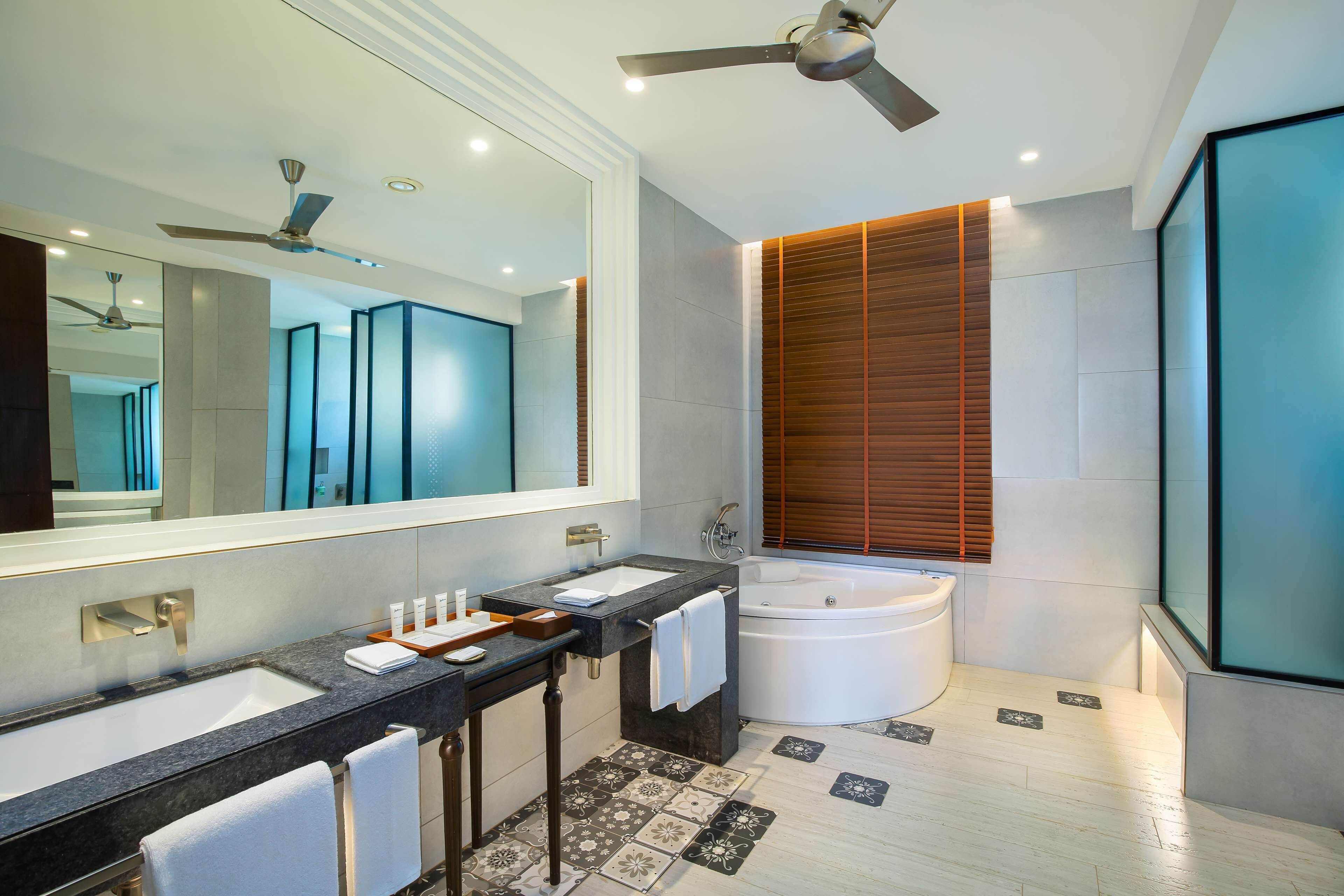 A modern bathroom with a dual sink vanity, a large mirror, a ceiling fan, and a freestanding bathtub.