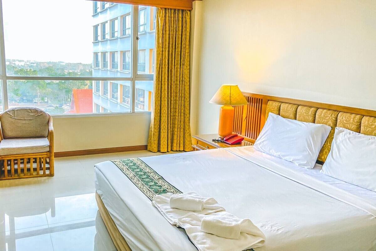 Une chambre d’hôtel avec un grand lit, une chaise, une table de chevet et une fenêtre avec des rideaux.