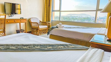 Habitación de hotel con dos camas, televisión, una silla y vista a la ciudad.