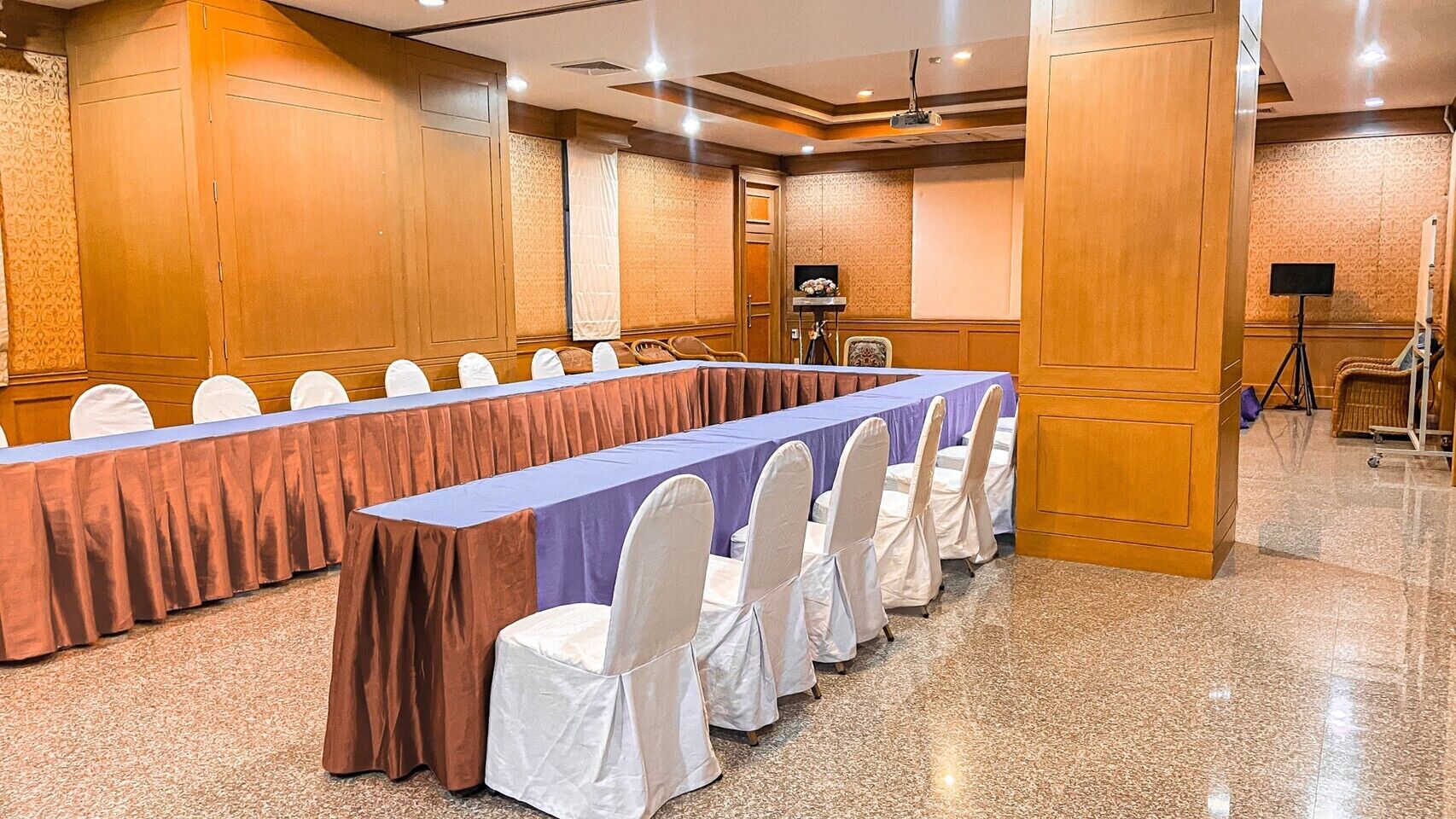Un salón de conferencias con una larga mesa, sillas blancas y un proyector.