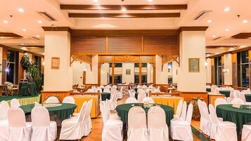 Un salón de banquetes con mesas redondas, sillas blancas y manteles verdes.